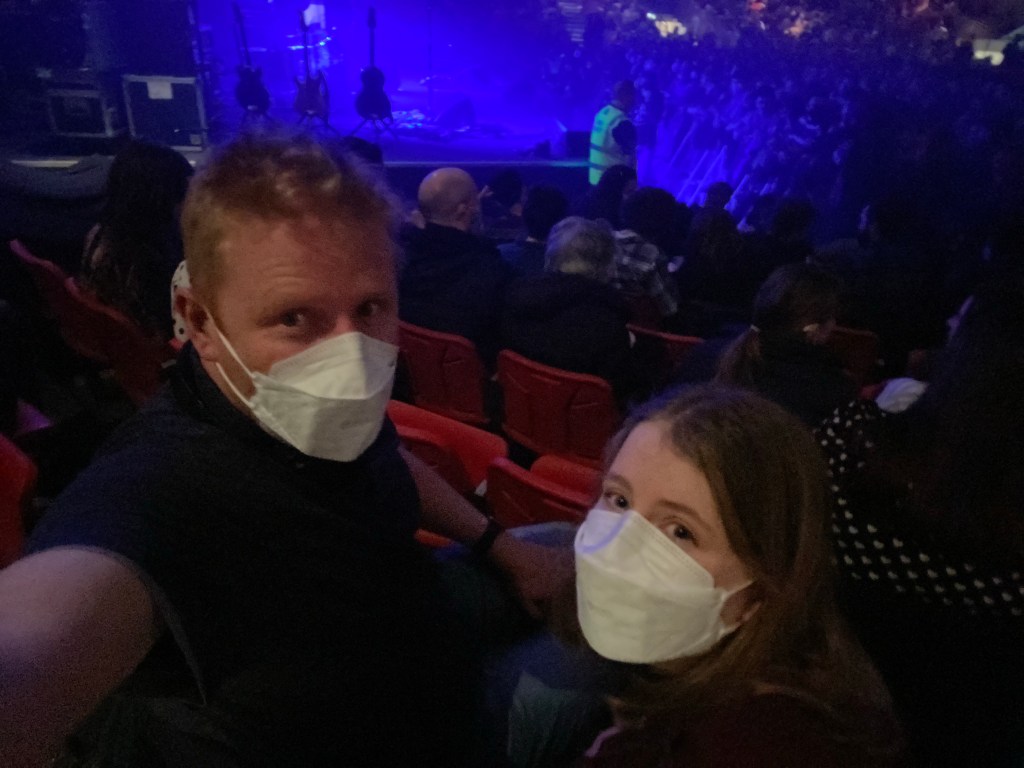 A man and girl in masks at a concert waiting for Big Thief to start