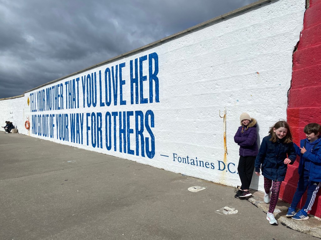 White wall with Fontaines DC lyrics in large all caps bold print