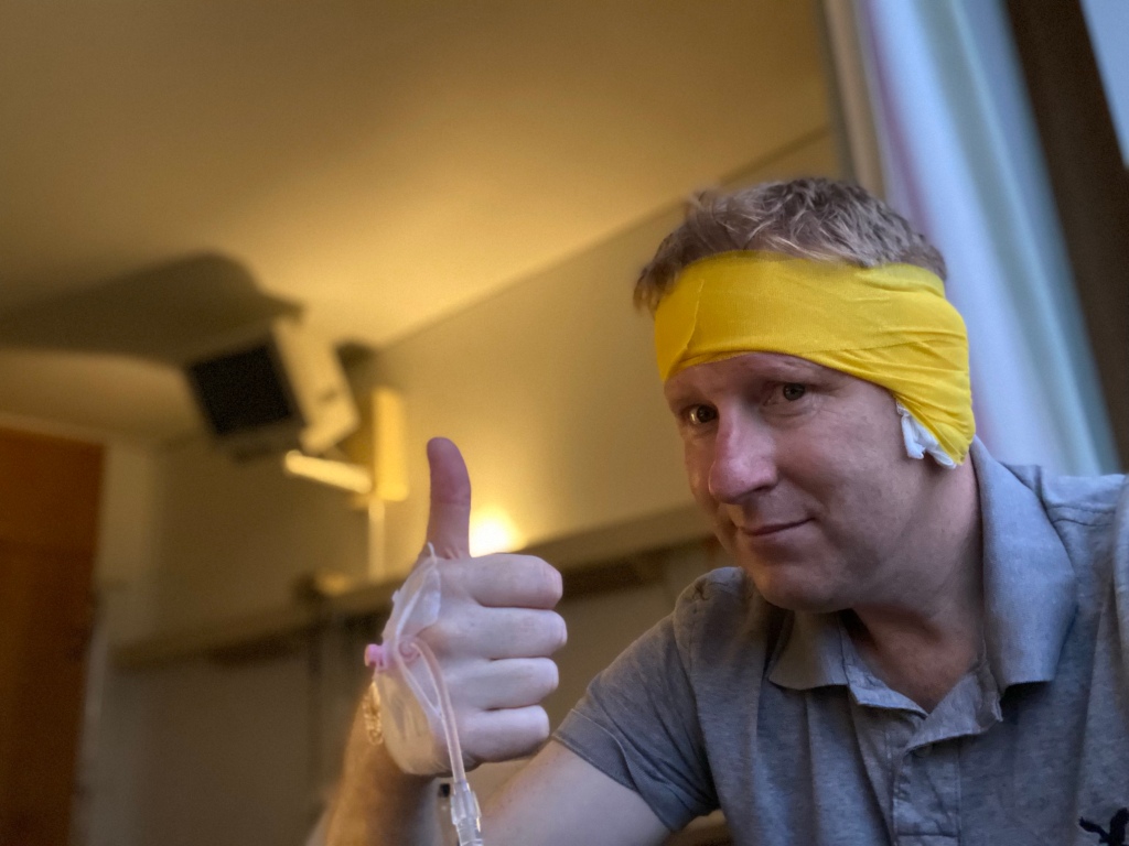 Man with mustard headband and ear dressing giving thumbs up