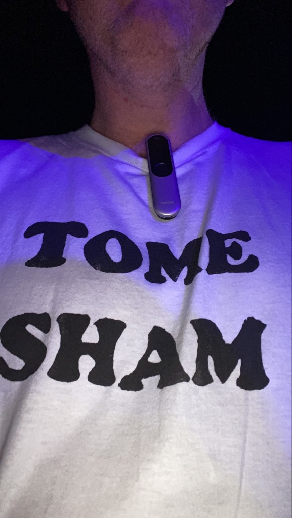 Roger On microphone clipped to a TShirt that says “Tome Sham”