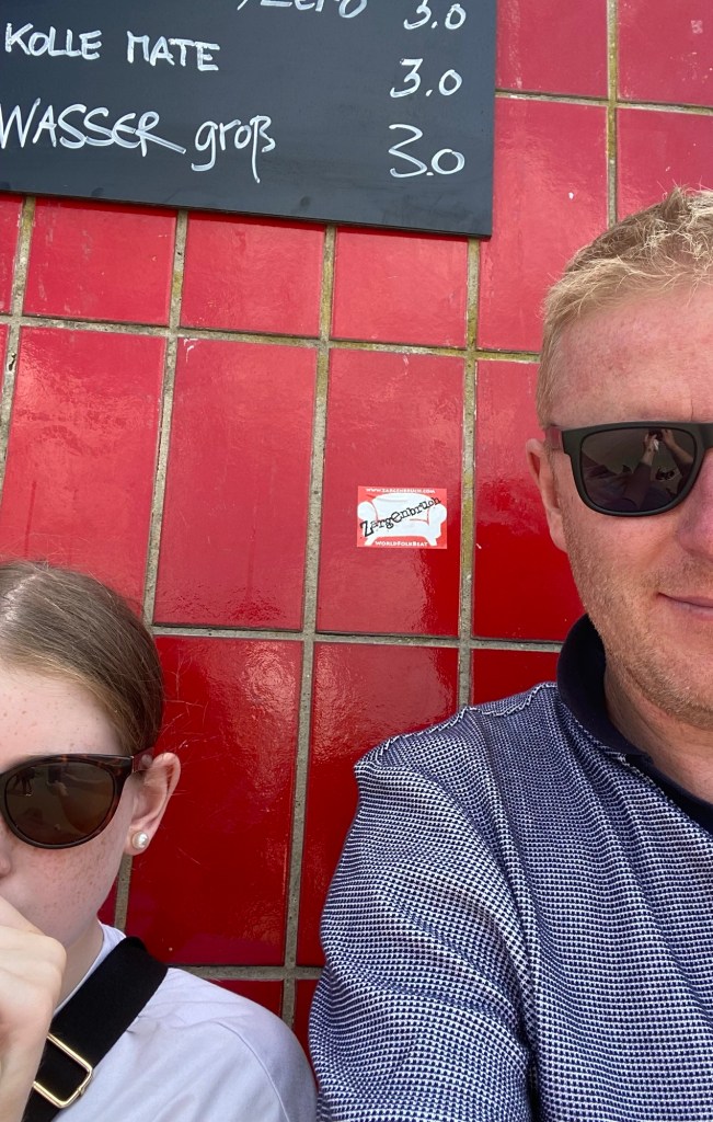 Man and girl in sunglasses sitting in front of red tiled wall. 