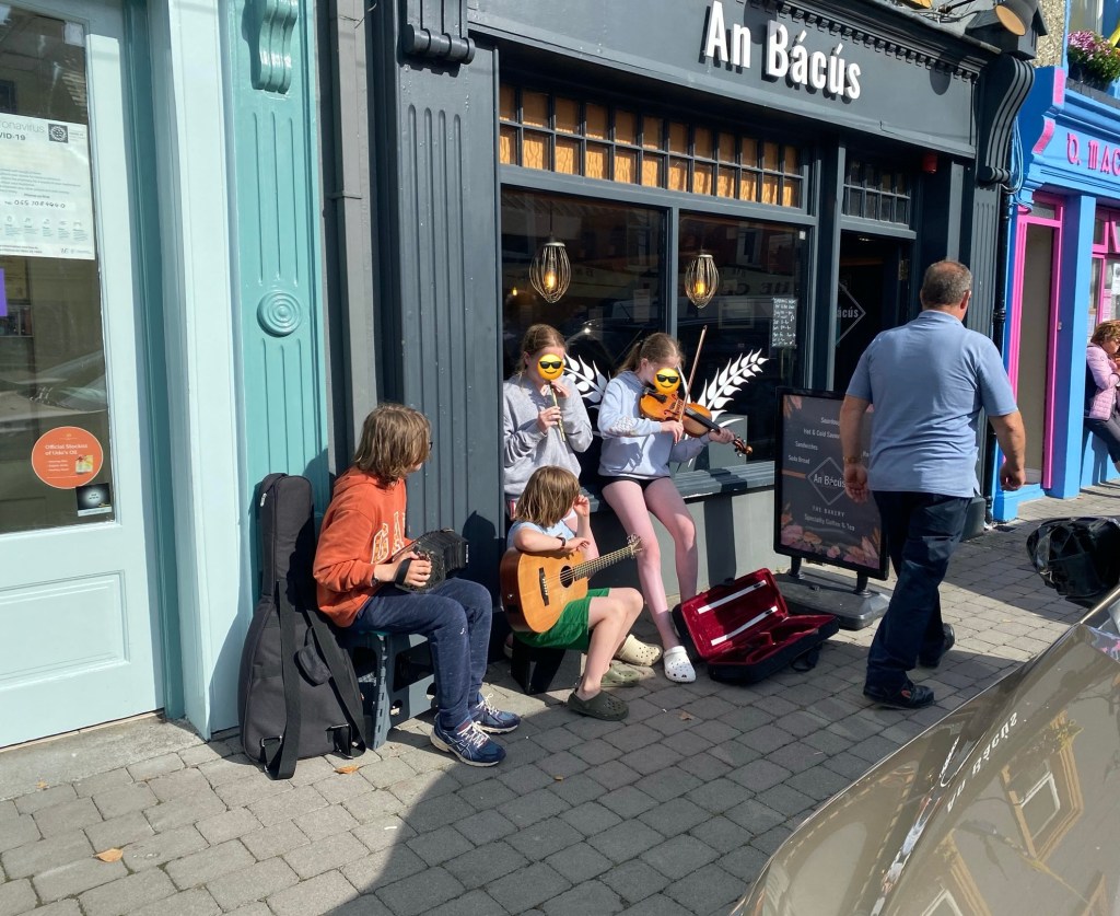 Children busking with concertina, guitar, tin whistle and violin outside bakery called An Bácús in Miltown Malbay Co Clare during the Willie Clancy Summer School
